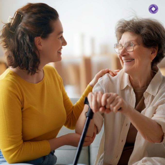 A young woman sits with and supports an older woman holding a cane.