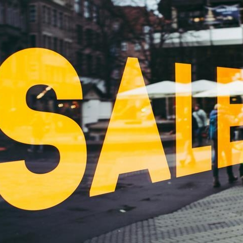 Yellow sale sign in storefront window urging shoppers to spend money