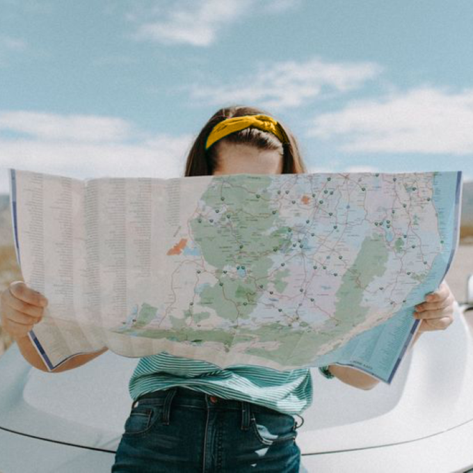 Woman on a budget friendly vacation seated on the hood of a car looking at a map