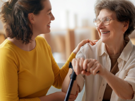 A young woman sits with and supports an older woman holding a cane.