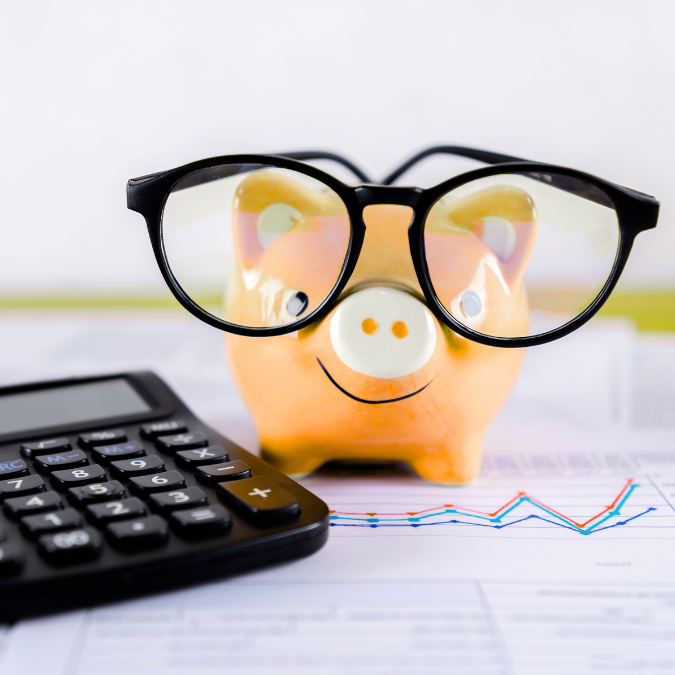 A photo of a yellow piggy bank wearing glasses next to a black calculator.