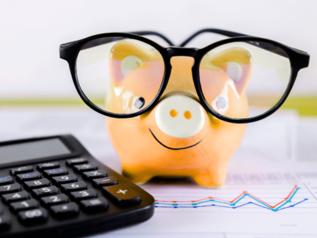 A photo of a yellow piggy bank wearing glasses next to a black calculator.